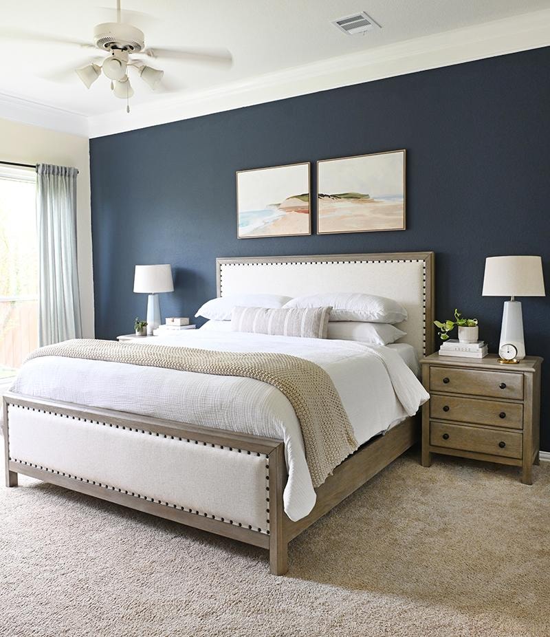 Primary bedroom with navy blue accent wall, upholstered bed, and wood nightstands