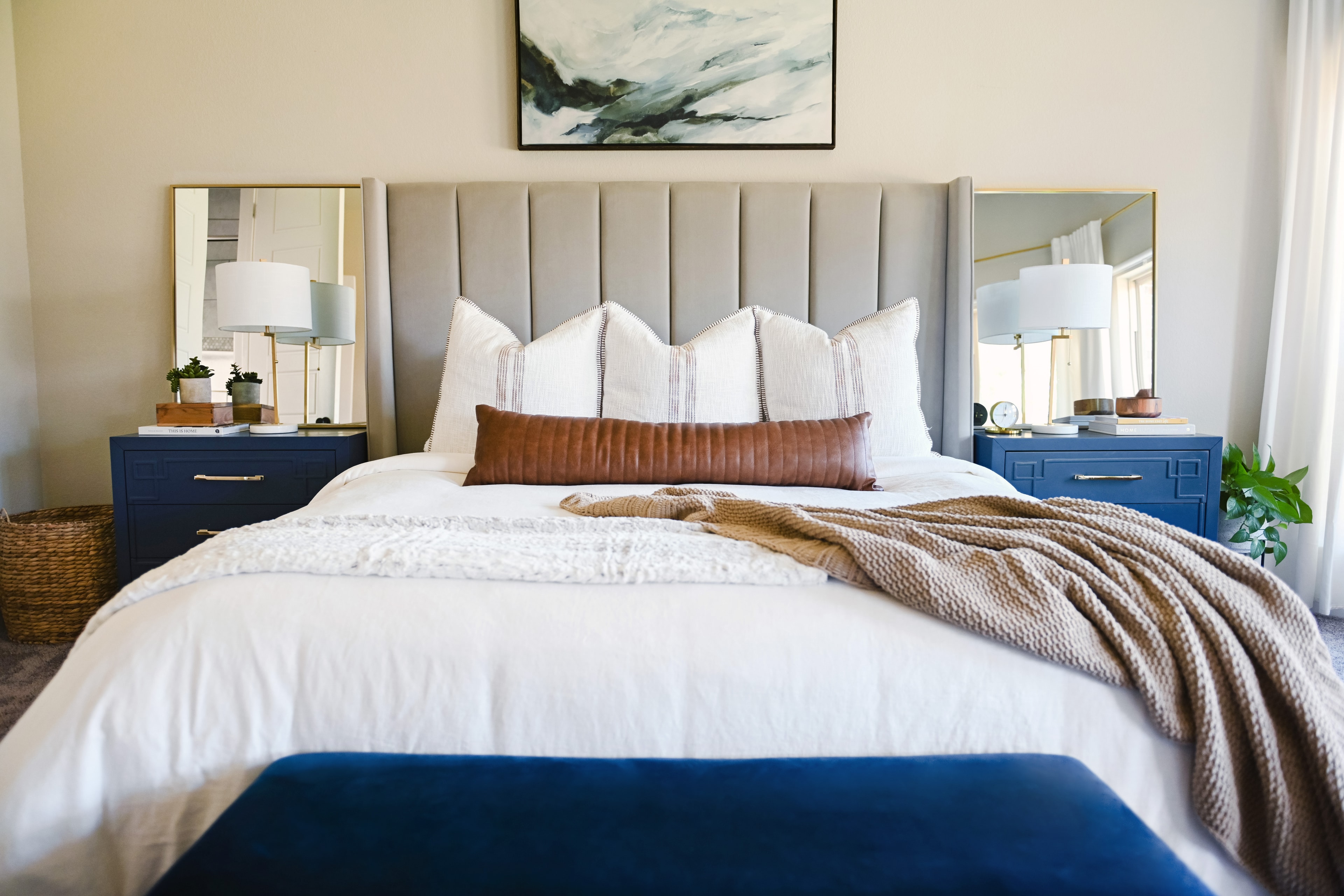 Primary bedroom with upholstered headboard, navy nightstands, and abstract art