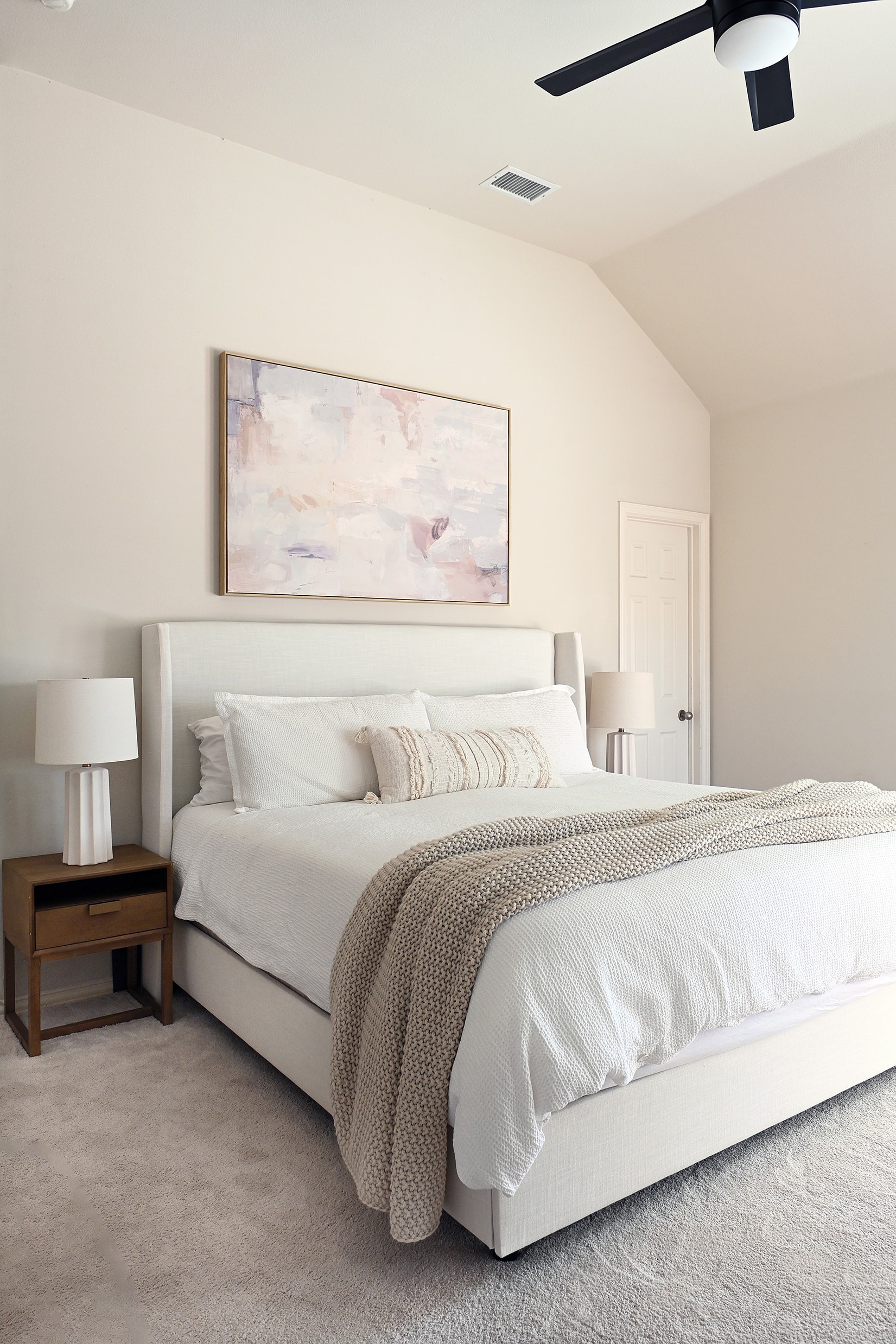 Primary bedroom with white upholstered wingback bed, abstract art, and wood nightstands