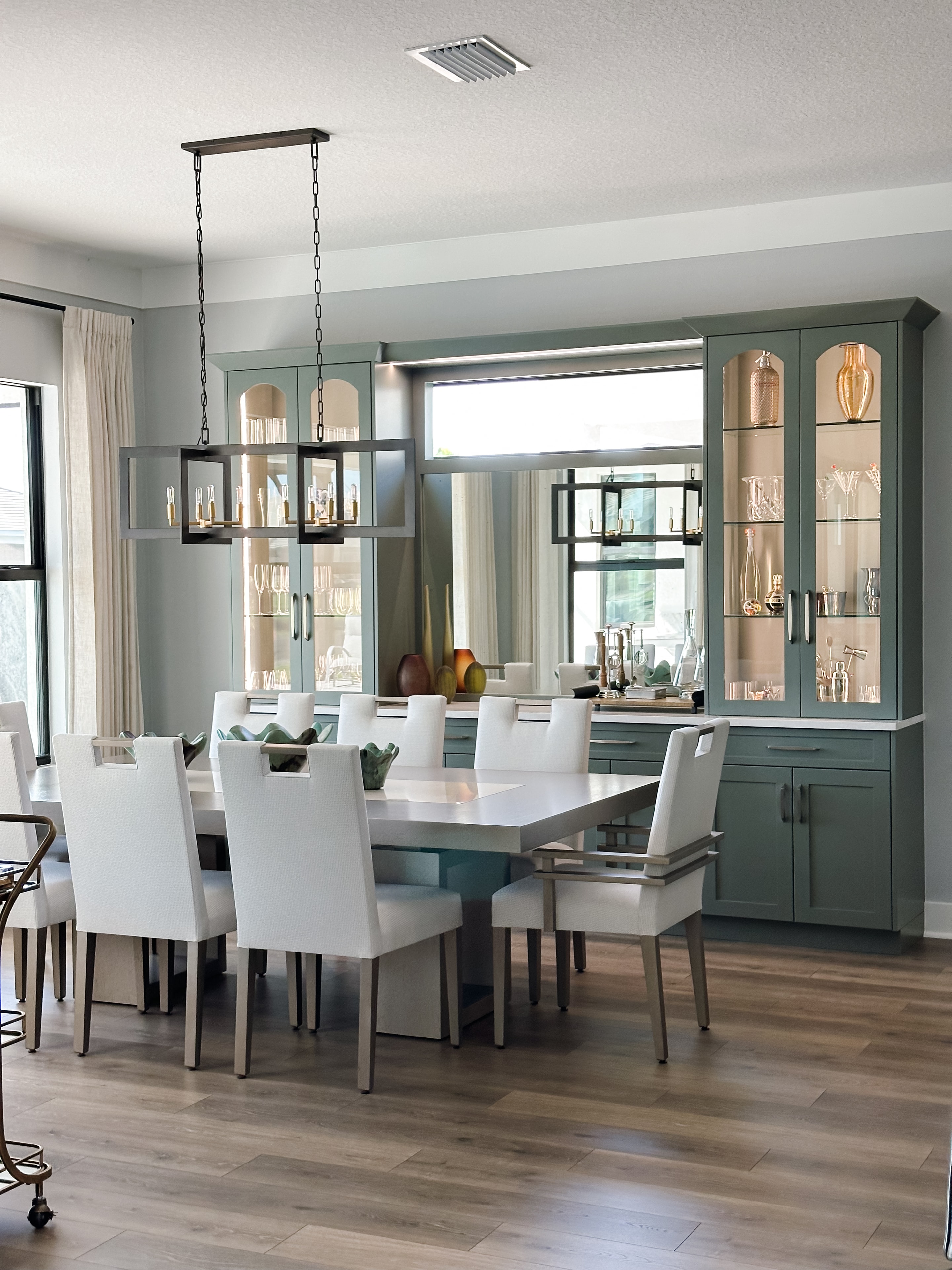 Dining room with sage green cabinetry, white upholstered chairs, rectangular table, and linear chandelier