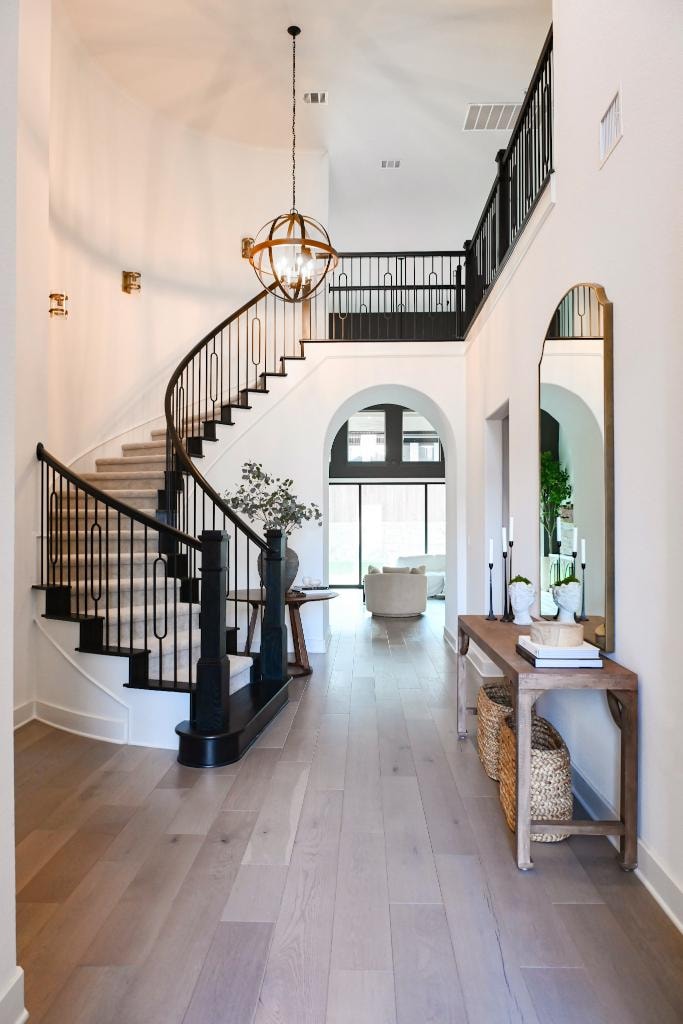 Grand entryway with curved staircase, globe chandelier, and arched doorway