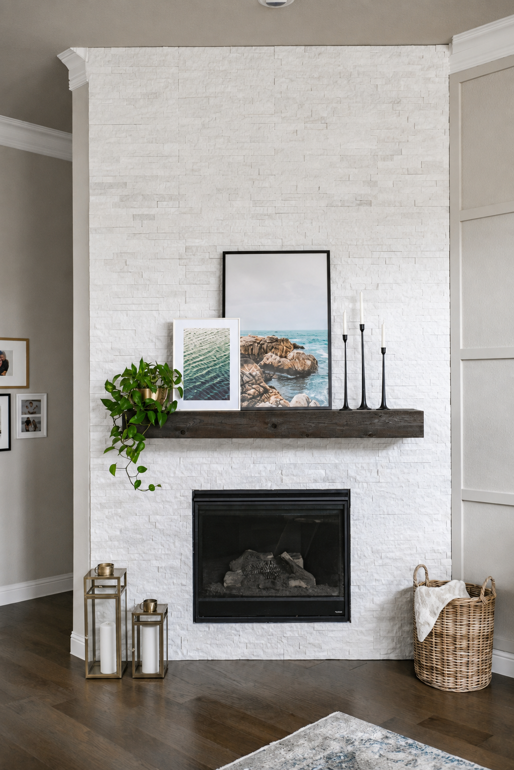 White brick fireplace with dark wood mantel, framed coastal art, trailing plant, and brass lanterns