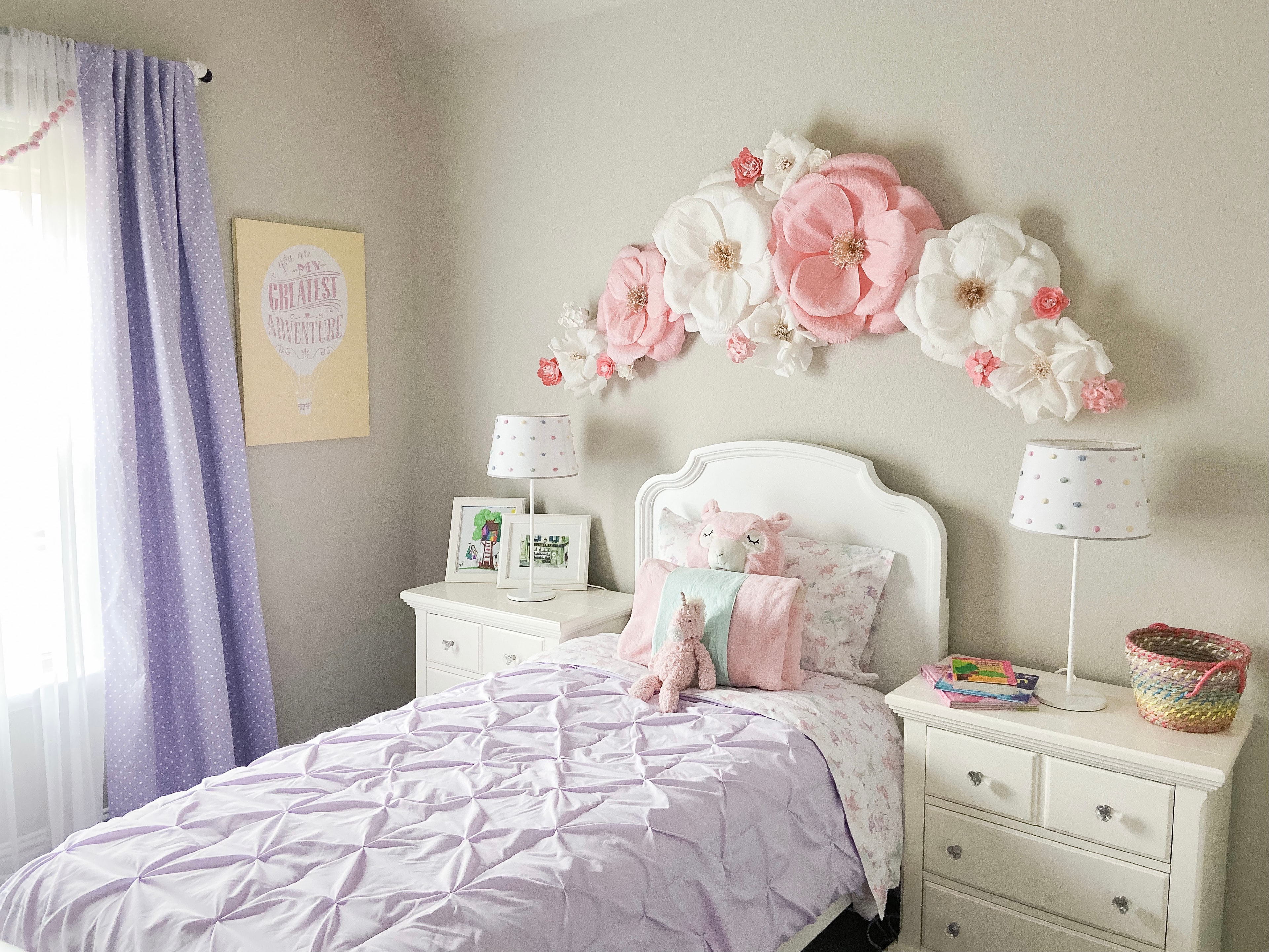 Girl's bedroom with paper flower wall art, lavender bedding, and white furniture