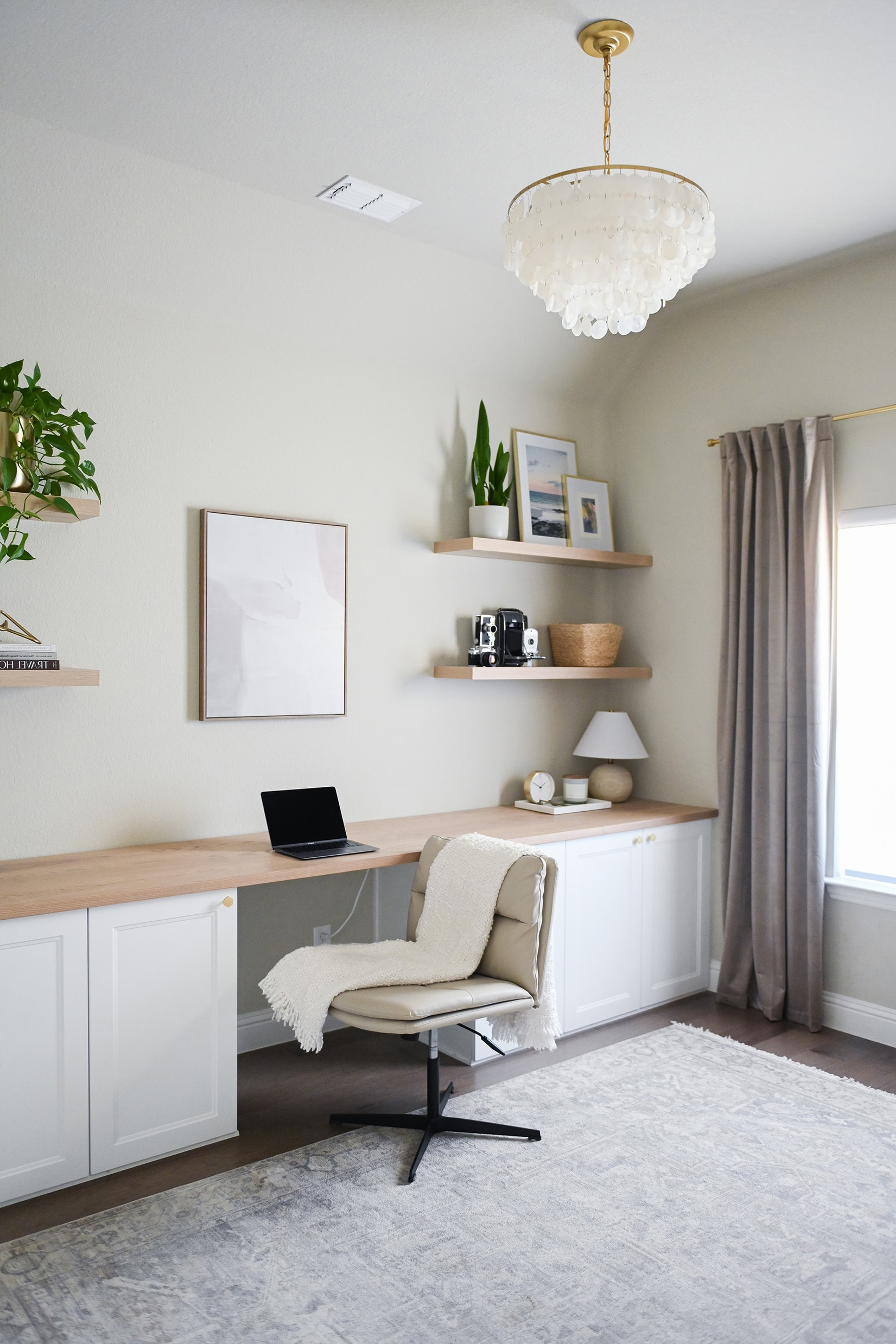 Home office with built-in white cabinetry, wood desk, floating shelves, and capiz chandelier