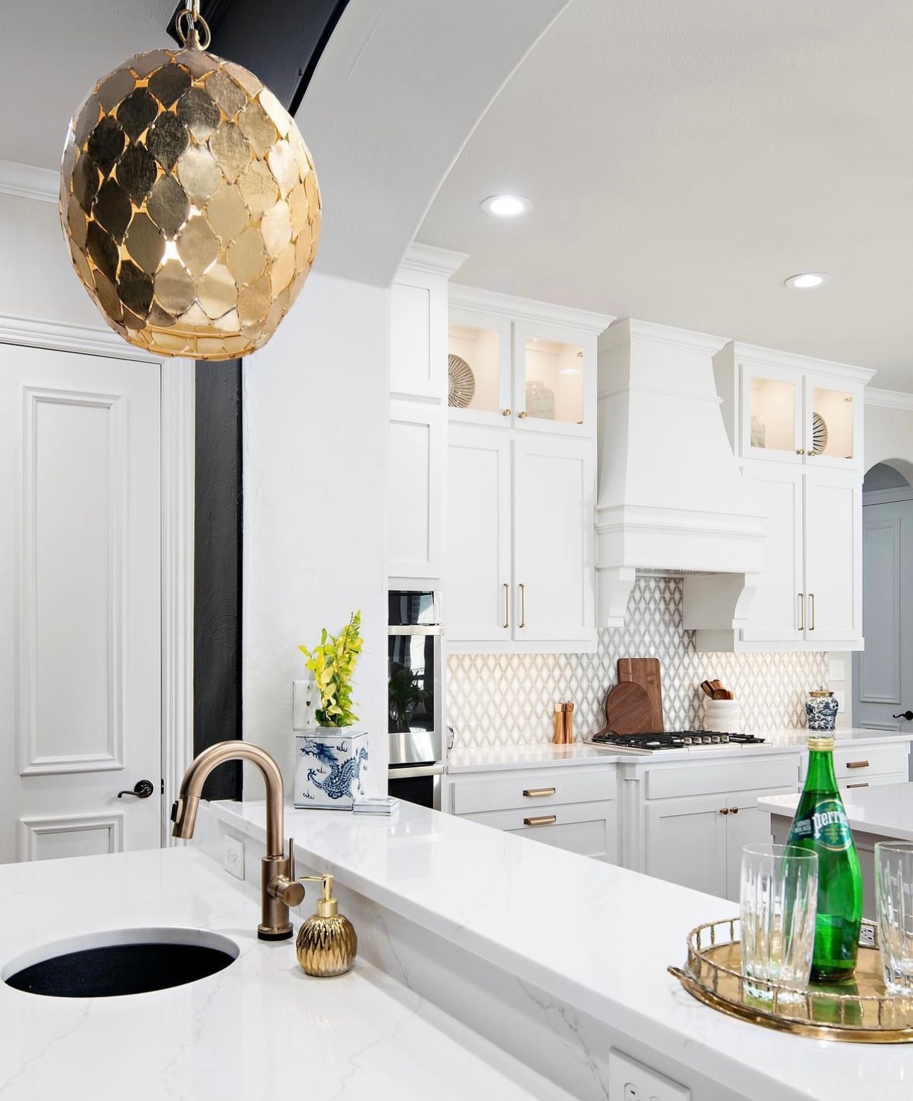 Kitchen with white cabinetry, gold globe pendant, marble countertops, and brass accents