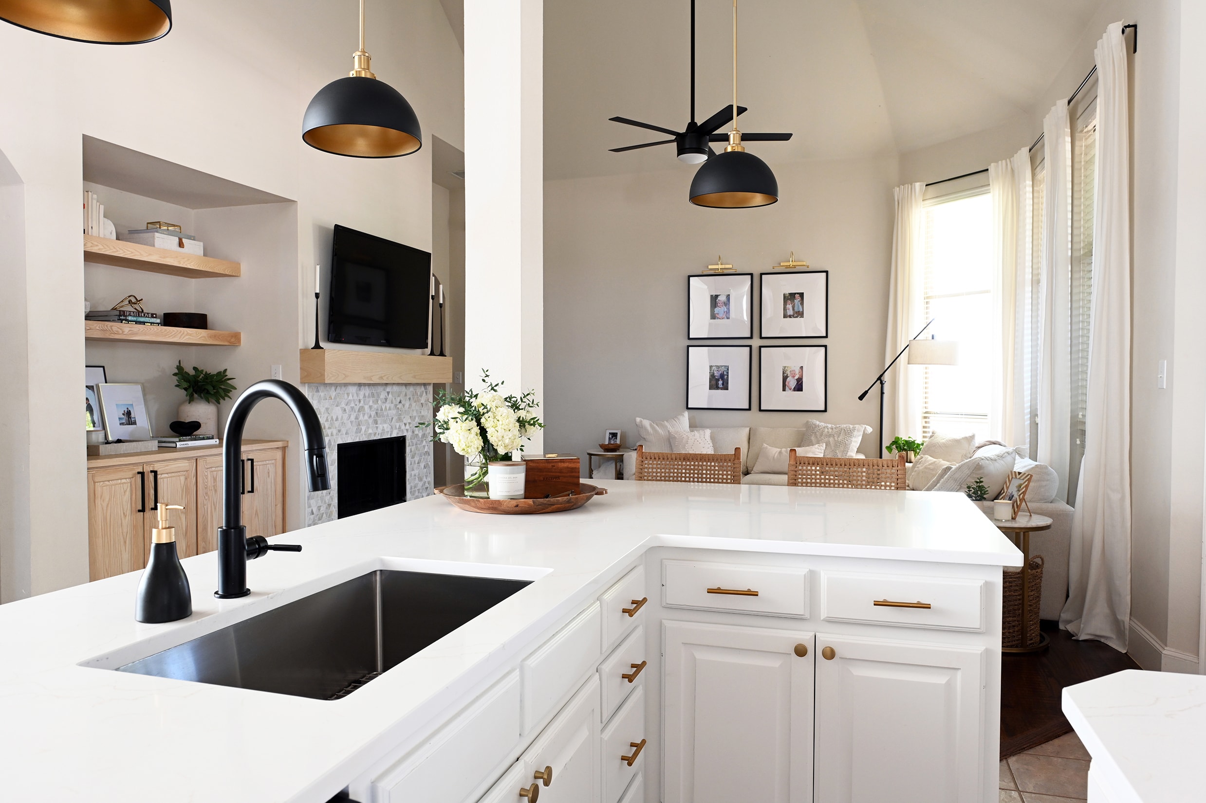 Open-plan kitchen and living room with white cabinetry, black pendants, and gallery wall