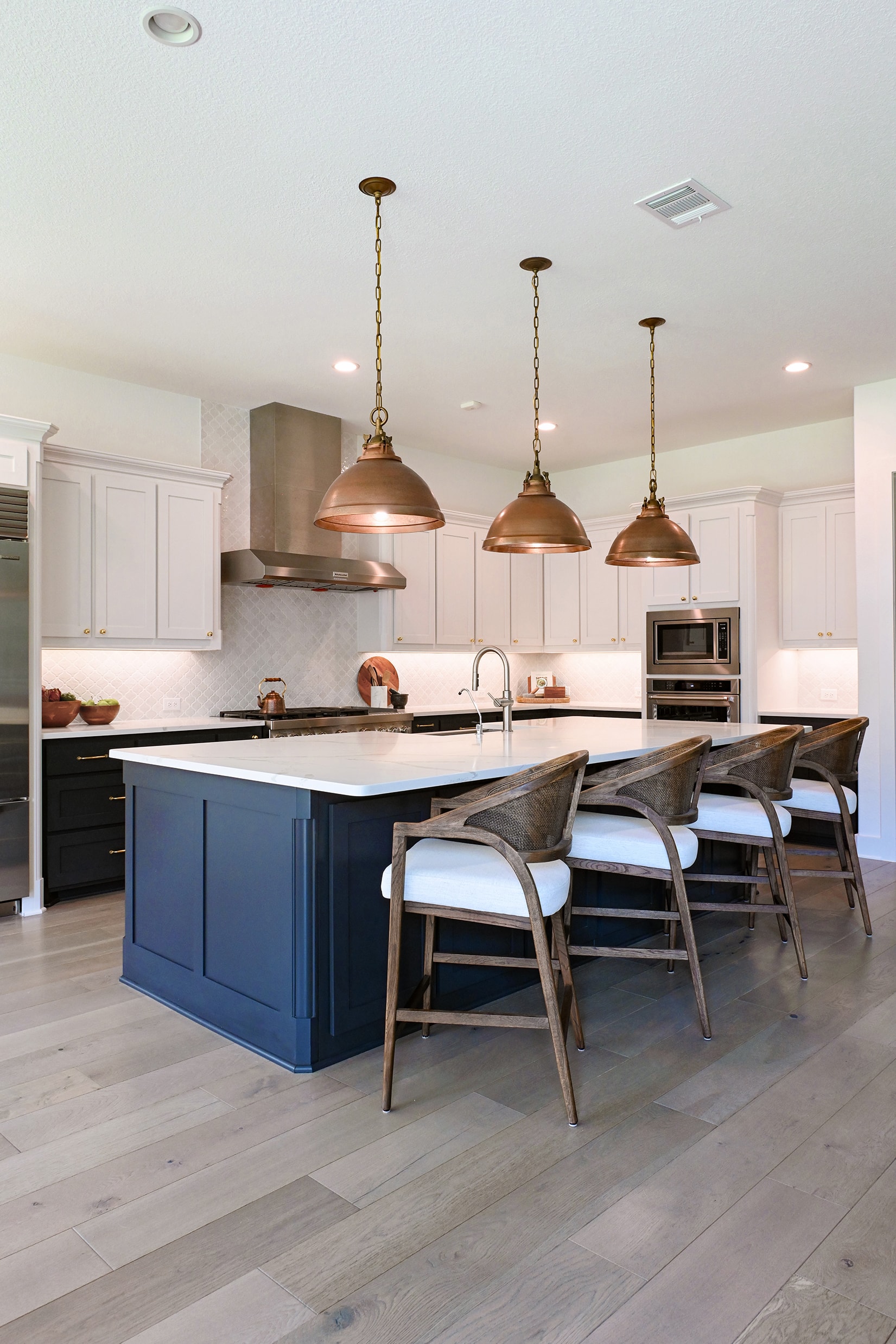 Kitchen with white cabinetry, navy island, copper pendant lights, and wood bar stools
