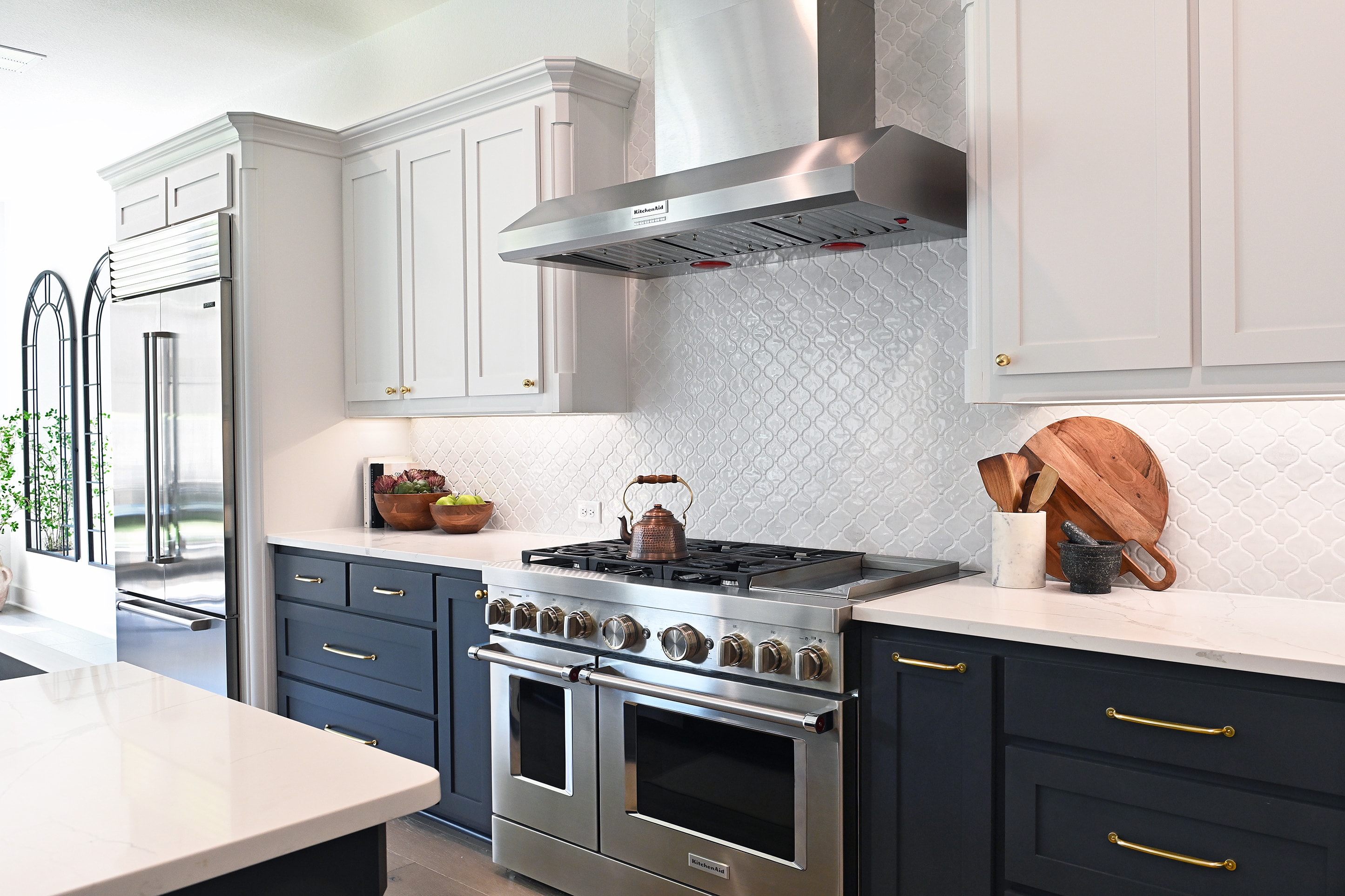 Kitchen with navy lower cabinets, white upper cabinets, arabesque tile backsplash, and professional range