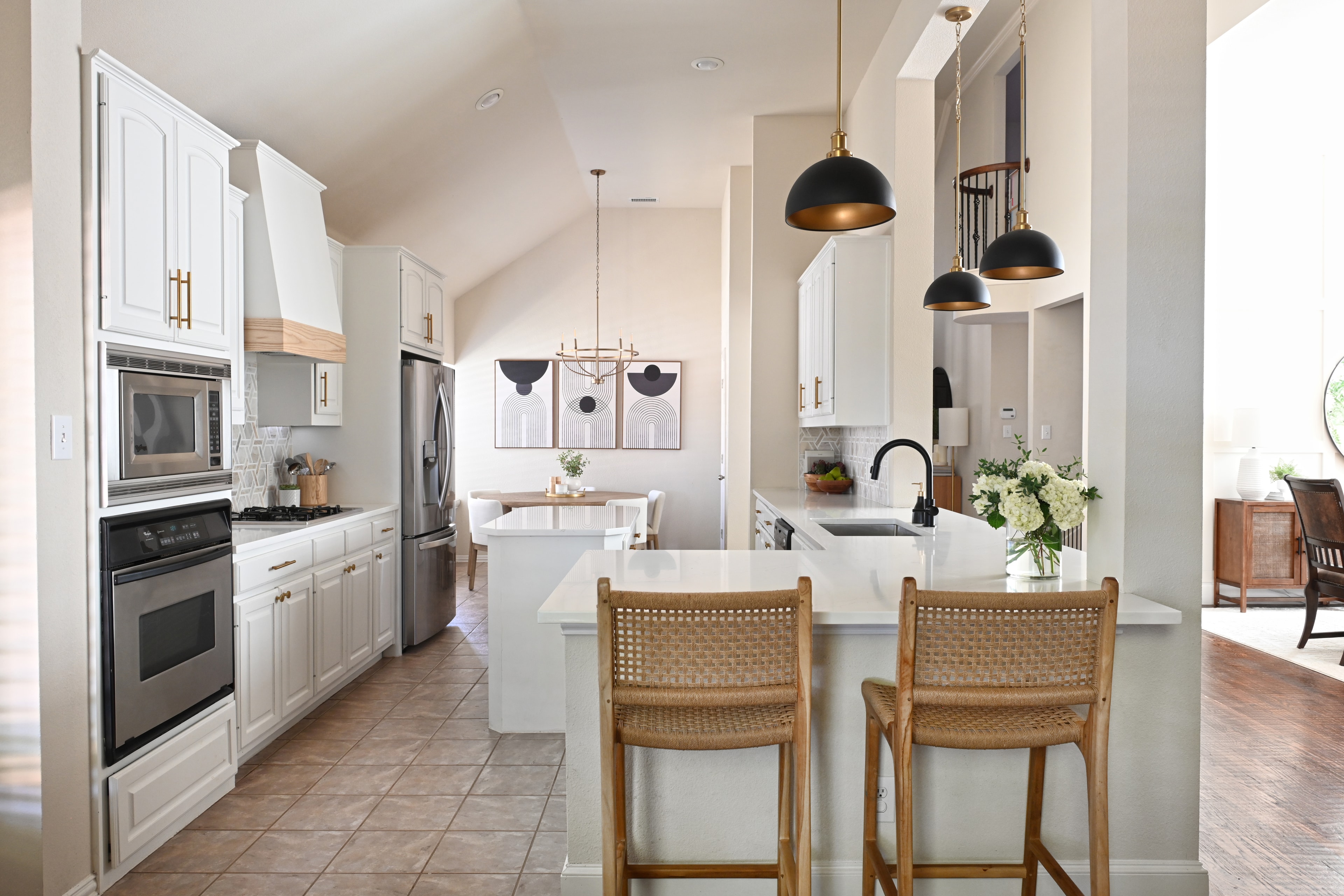 Kitchen with white cabinetry, brass hardware, cane bar stools, and abstract art