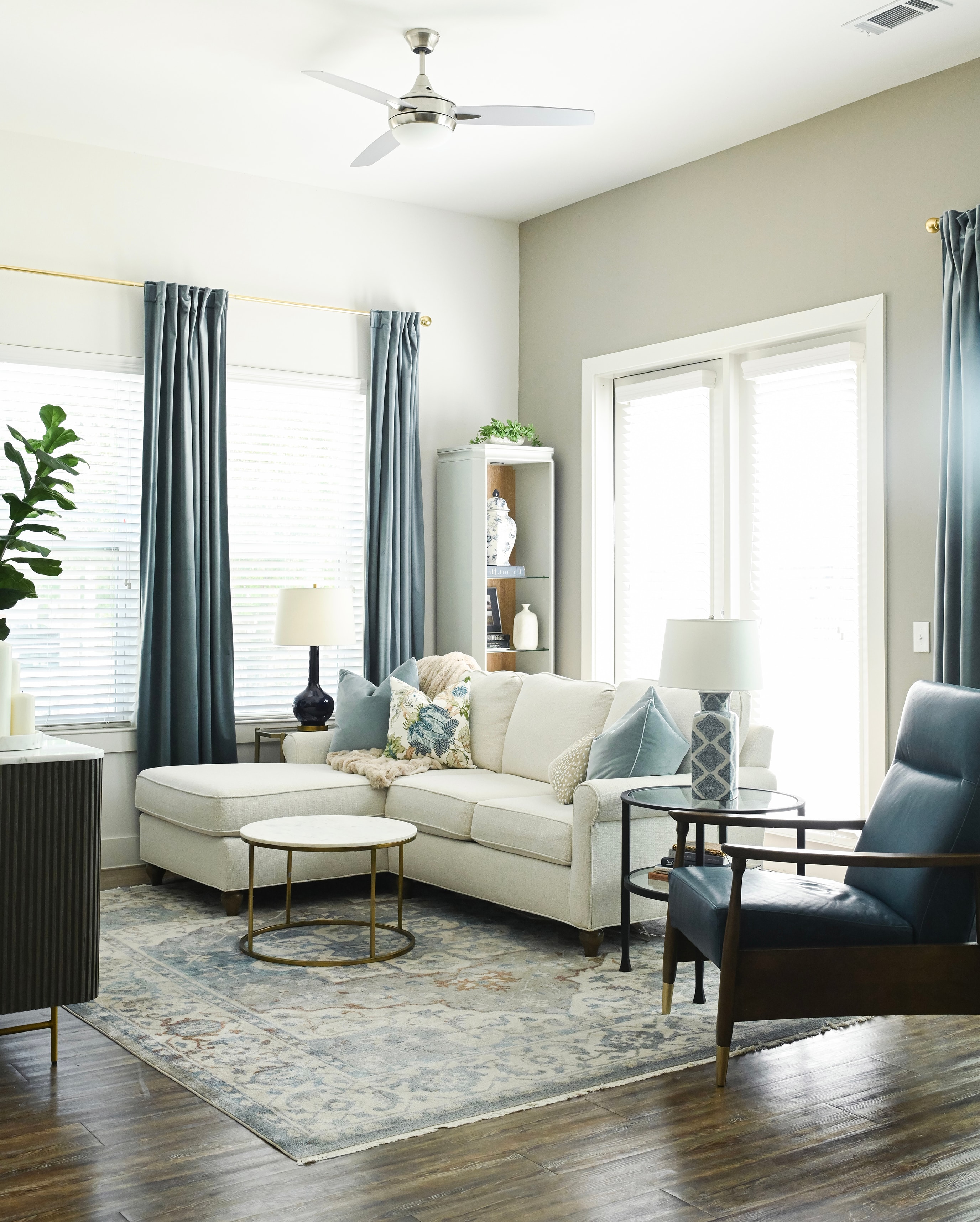 Living room with cream sectional, blue velvet curtains, and brass hardware