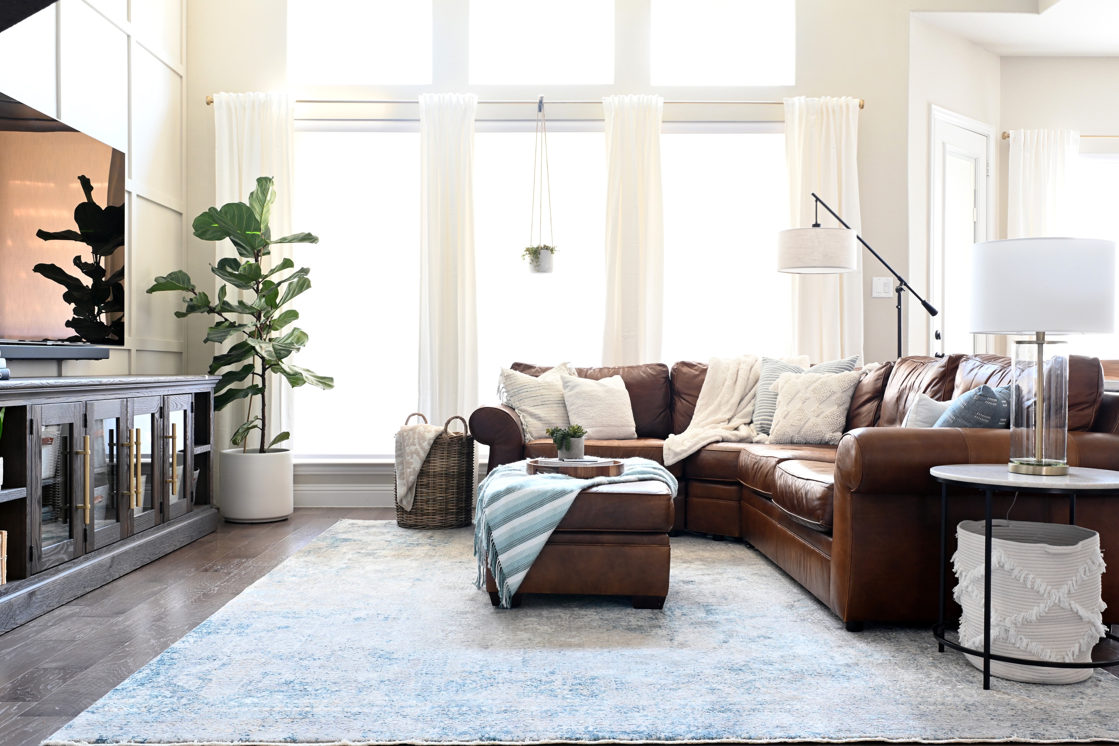 Bright living room with brown leather sectional, fiddle leaf fig, and large windows