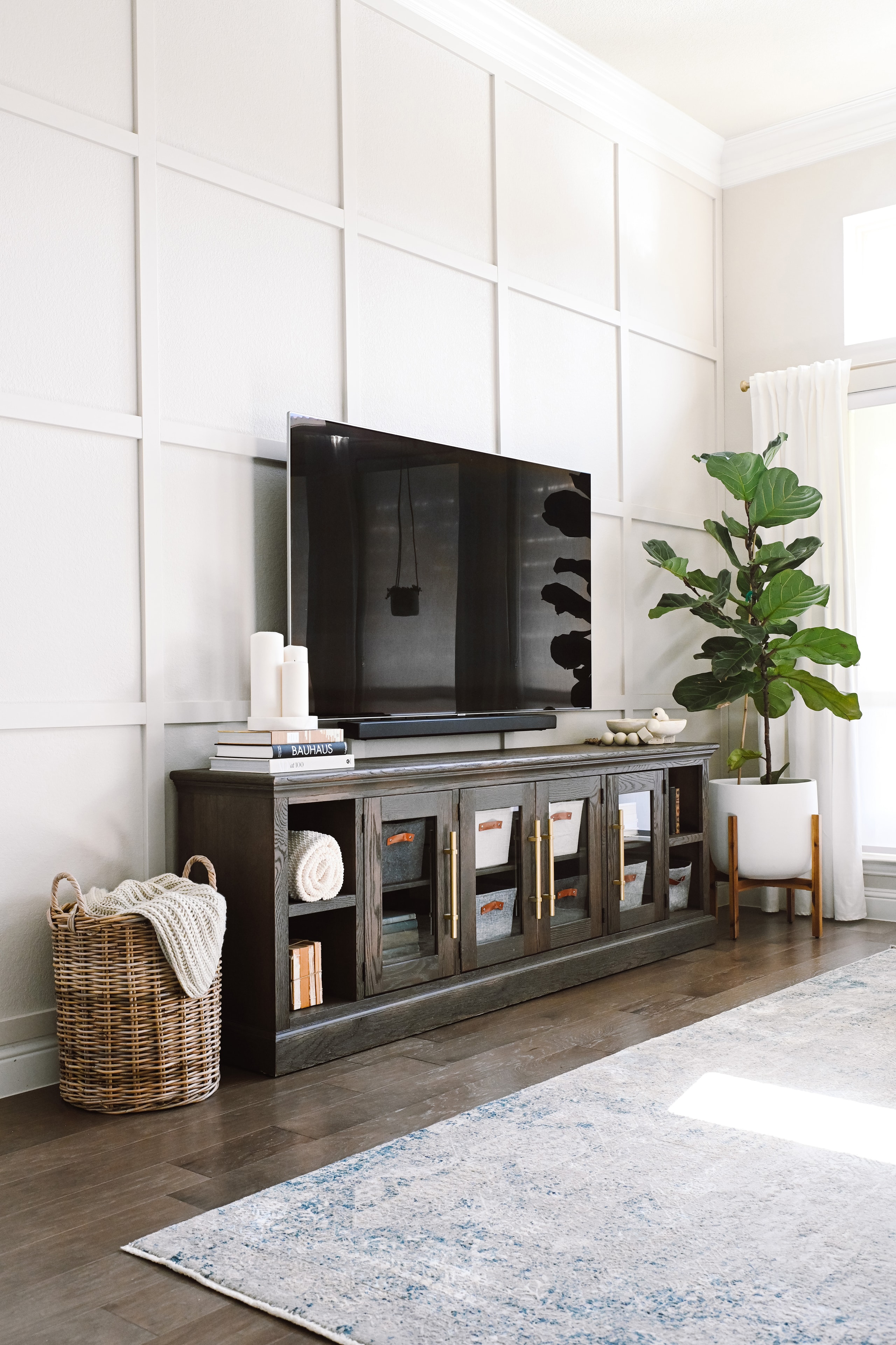Living room with dark TV console, board-and-batten wall, and fiddle leaf fig
