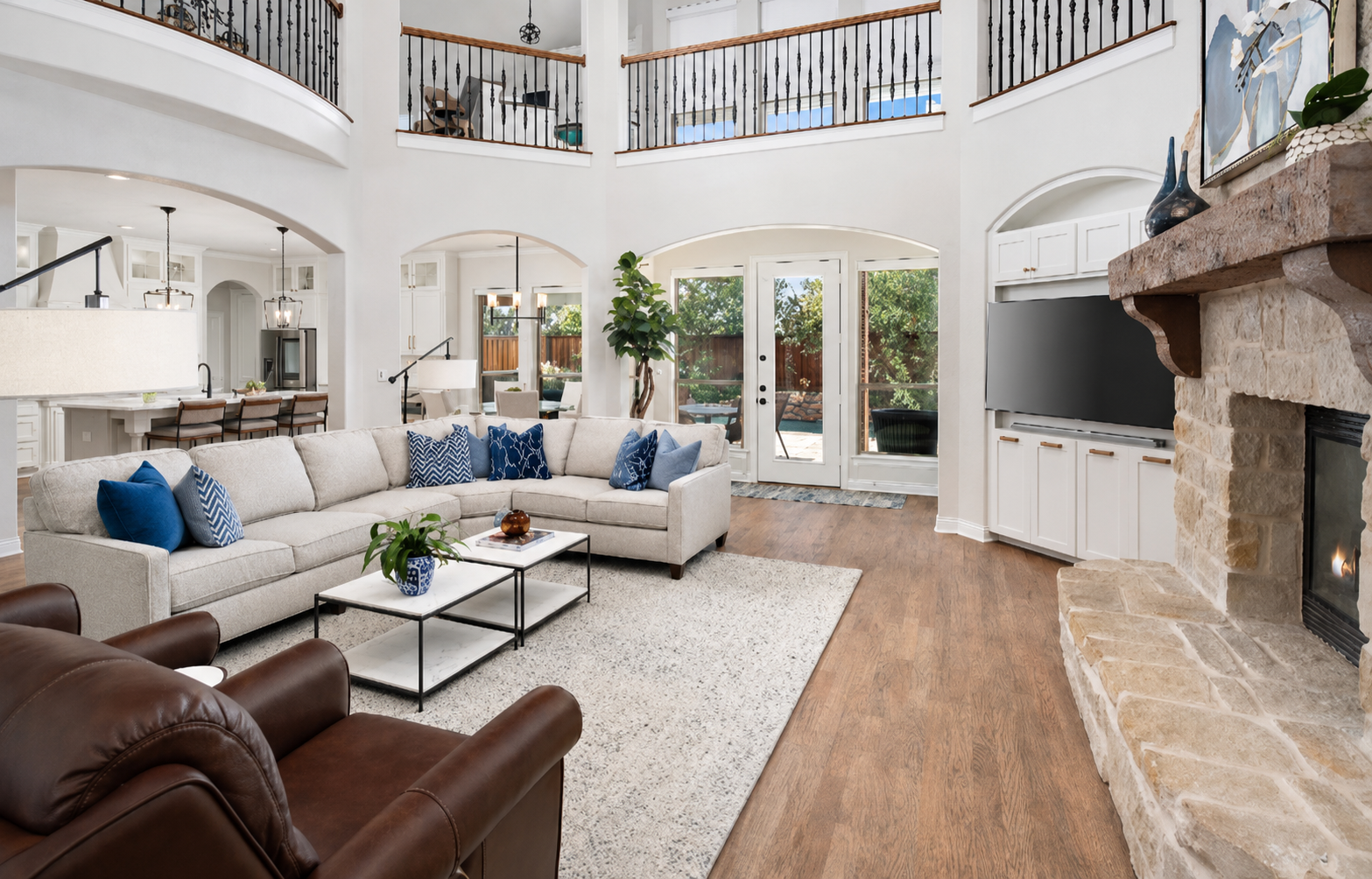 Bright two-story living room with stone fireplace, sectional sofa, and open-plan kitchen