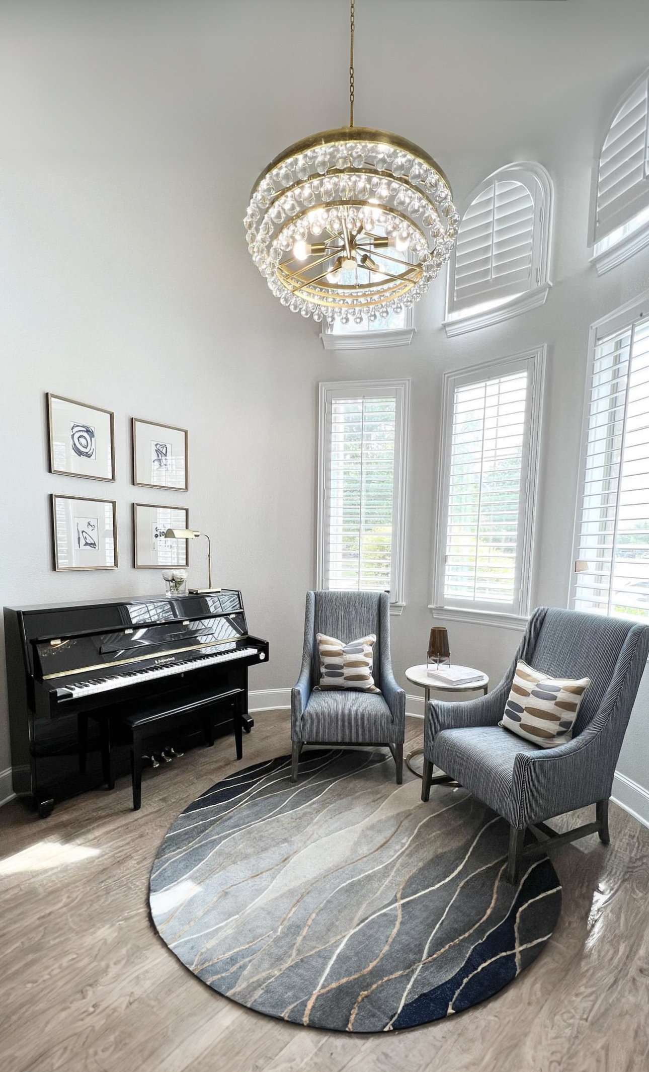 Music room with upright piano, crystal chandelier, and two wingback chairs on a round rug