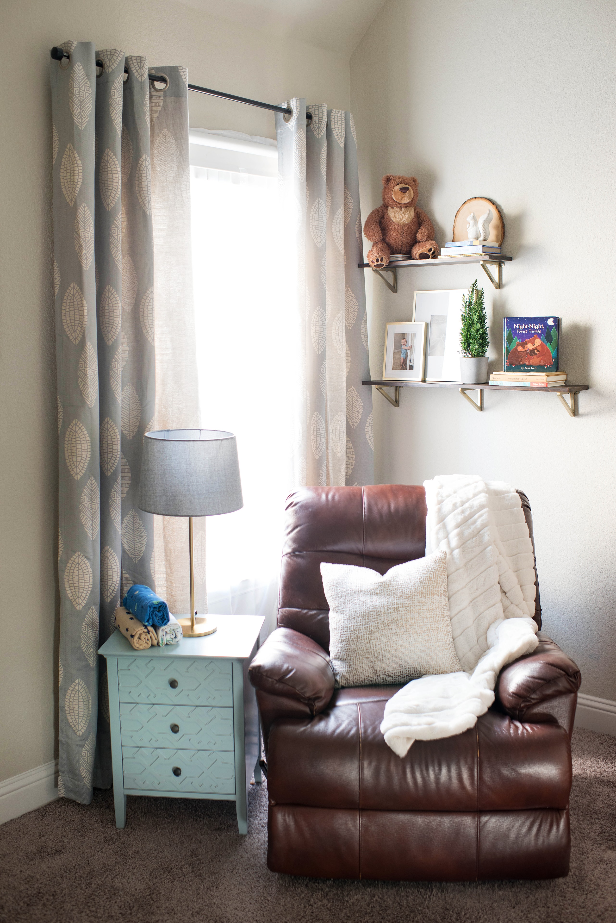 Cozy nursery reading nook with leather recliner, patterned curtains, and styled shelving